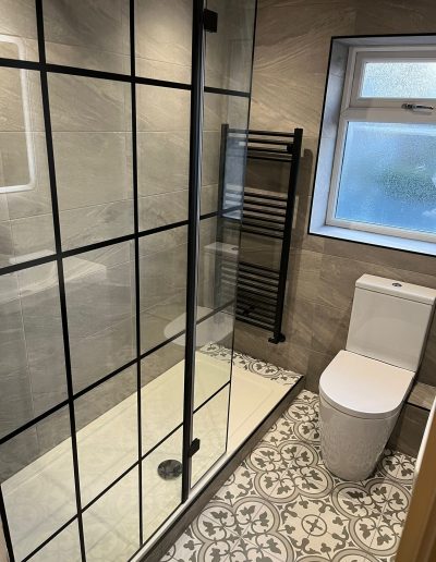 Walking in shower with black frame, heated towel rail at the end of the shower, with white toilet situated next to the right.