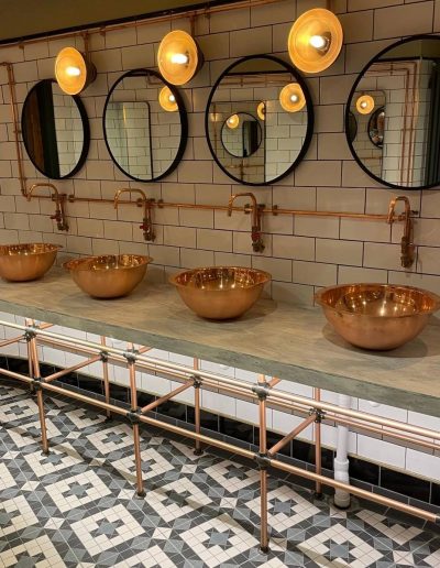 Four chrome bowl wash hand basin with circular mirrors above, situated in a drinking establishment.